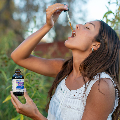 woman in nature taking a more milk special blend tincture in her mouth