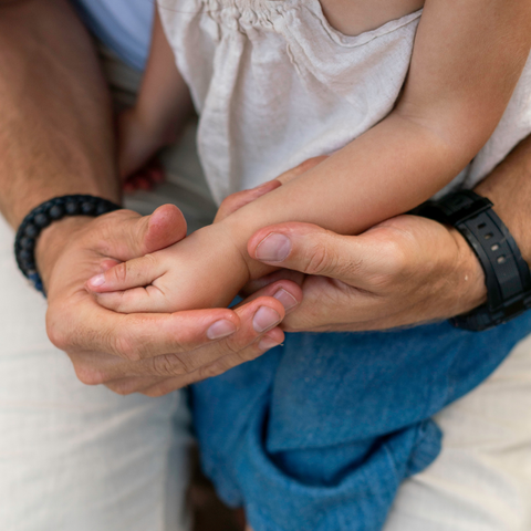 Close-up of adult hands holding a child's hand, with a focus on the interaction between the two.
