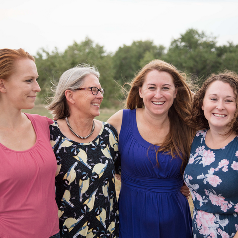 Founder, Kathryn Higgins, with her 3 daughters standing in nature with arms around each other smiling. 