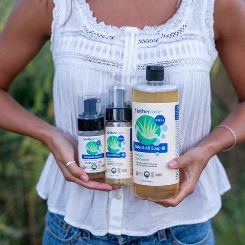 Person holding Motherlove baby and all soap bottles outdoors