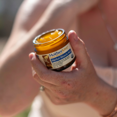 Hand holding a jar of Motherlove Herbal Muscle Relief Balm.