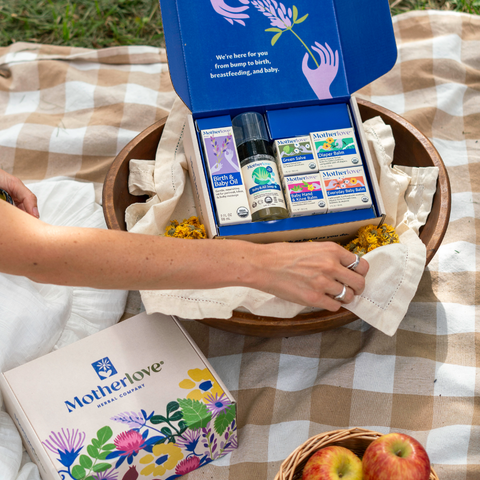 Motherlove product box on a picnic blanket with apples and a basket