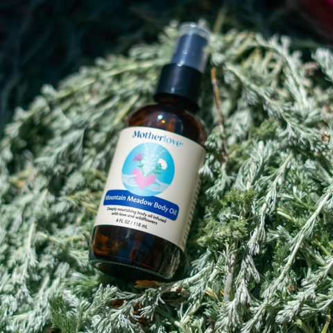 A bottle of Motherlove Mountain Meadow Body Oil resting on a bed of dried prairie sage and foliage.