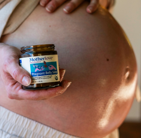 Pregnant person holding a jar of Motherlove Pregnant Belly Balm against their belly.
