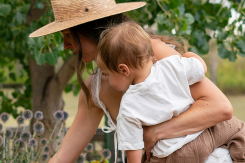 Woman holding a child in a garden with greenery and flowers in the background