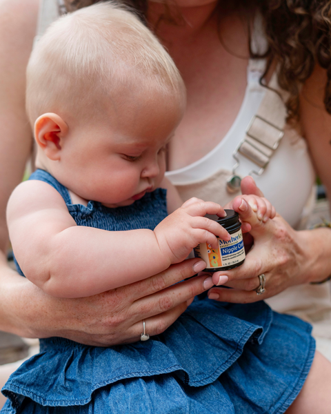 mom and baby holding nipple cream jar, wearing denim dress 