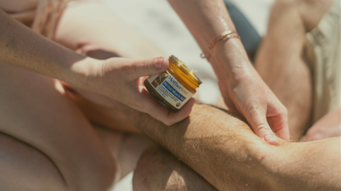 Person applying a jar of muscle rub to their leg.