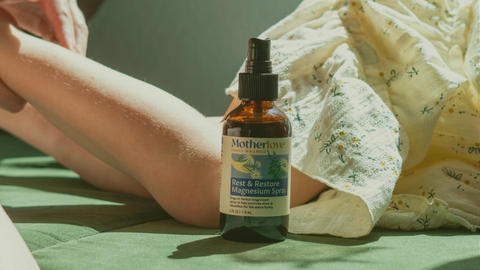 Bottle of 'Motherlove' magnesium spray on a green surface with a person lying down.