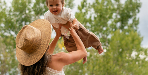 Woman holding a baby in a field with trees in the background