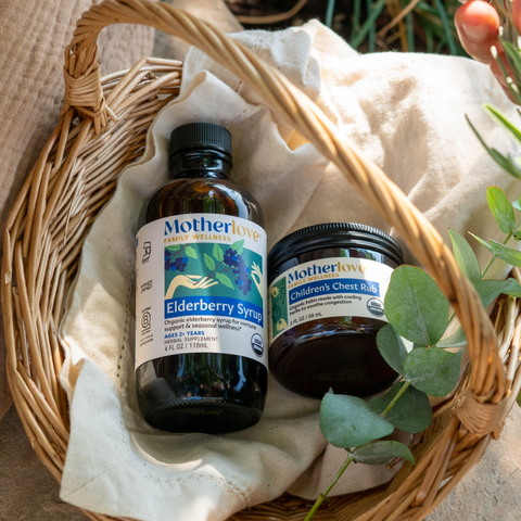 Bottle of Motherlove Elderberry Syrup and jar of Children's Chest rub in a basket with linen cloth